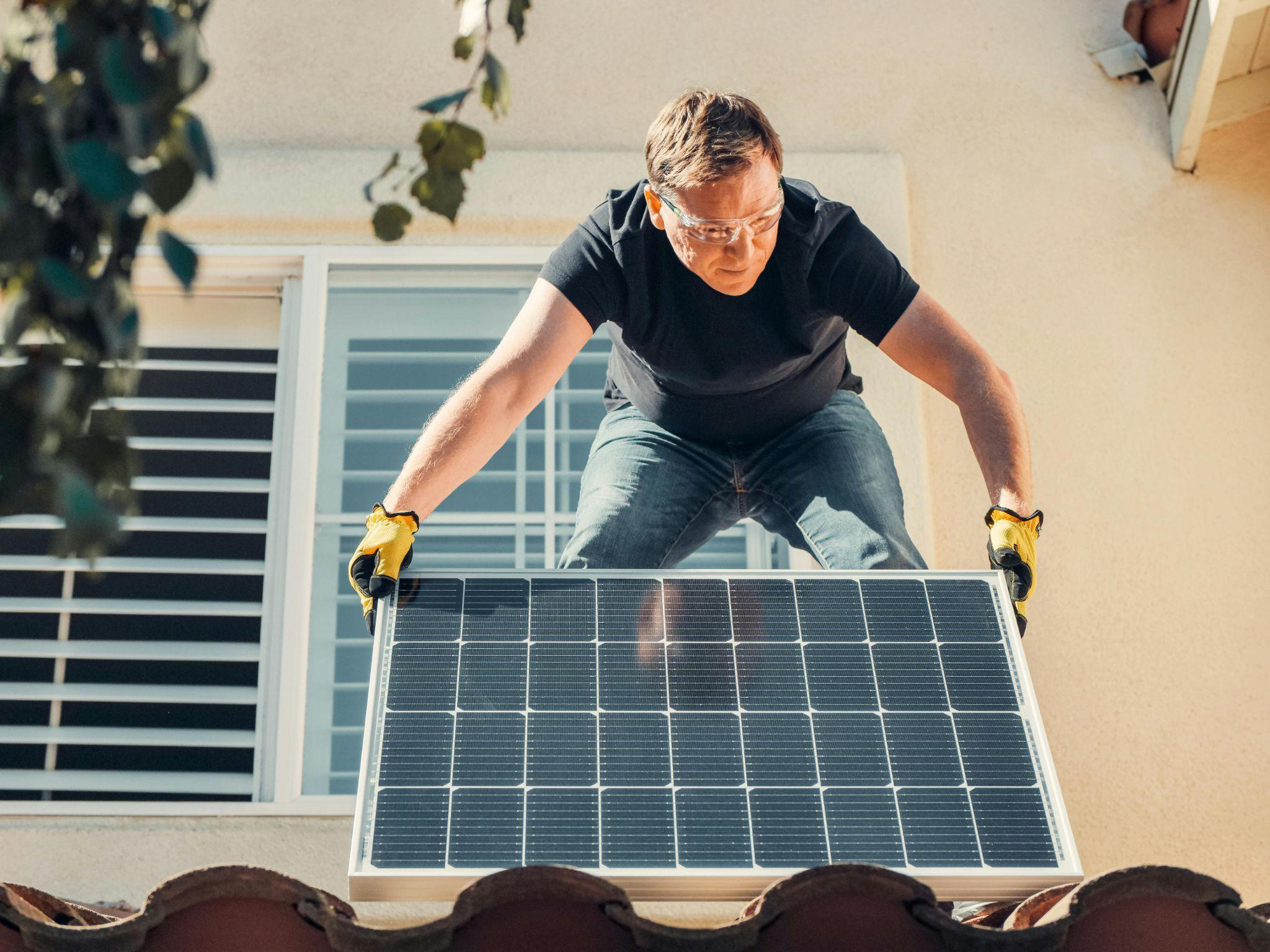 Homeowner lifting a solar panel onto a residential roof