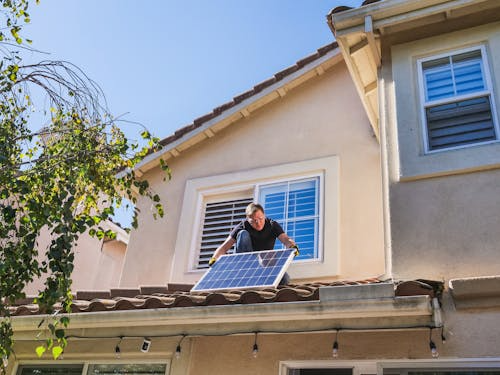 Technician removing an old solar panel from a residential rooftop for replacement.