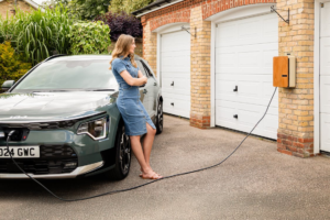 Young woman charging her electric vehicle at a home EV charging station outside her house.