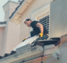 a roofer working on a home with solar panels removed and stacked on the ground