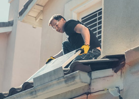 a roofer working on a home with solar panels removed and stacked on the ground