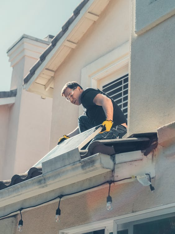 a roofer working on a home with solar panels removed and stacked on the ground