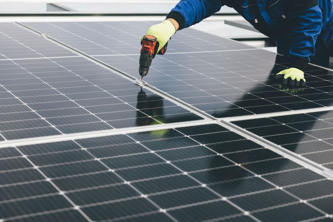 Technician using a power tool to repair solar panels on a rooftop.