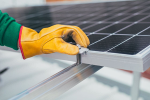 Close-up of a worker's gloved hand adjusting a bolt on a solar panel mounting system.